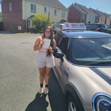 Young woman holding a certificate next to a parked car in a residential area.