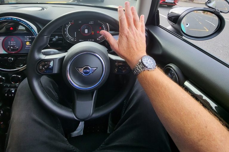 A driver's hand raised, resting on a steering wheel inside a car.