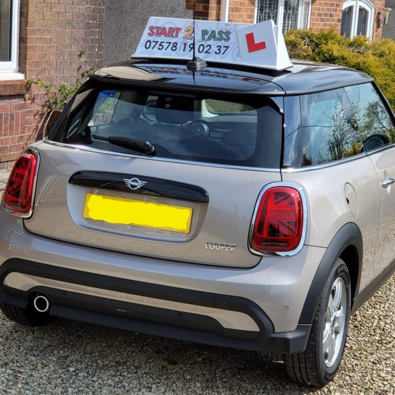 Silver Mini Cooper with a learner driver sign on the roof parked outside a house.