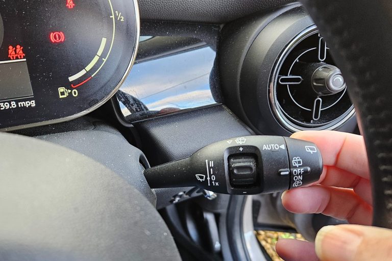 A hand using a car indicator stalk with dashboard visible in the background.