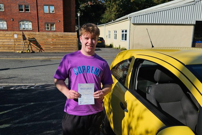 Young man in a purple shirt holding a paper, standing next to a yellow car.