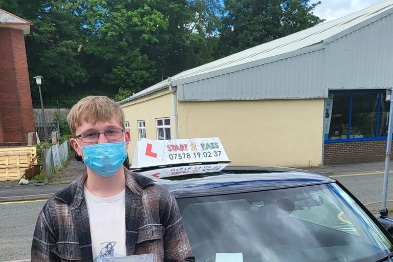 Young man wearing a mask holds a driving test certificate next to a learner car.