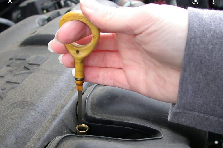 Hand holding a yellow dipstick above a car engine oil reservoir.