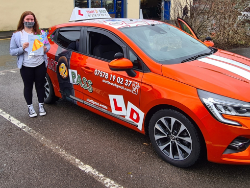 A smiling instructor stands next to a bright orange driving school car.