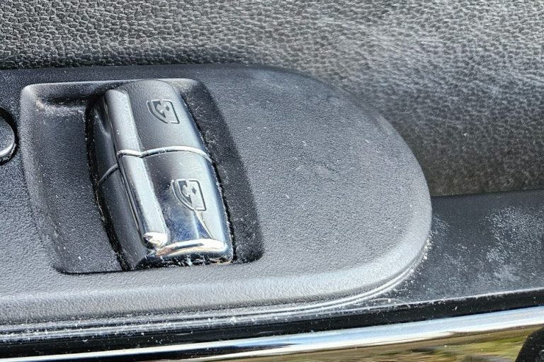 Close-up of a car window control switch on a textured surface.