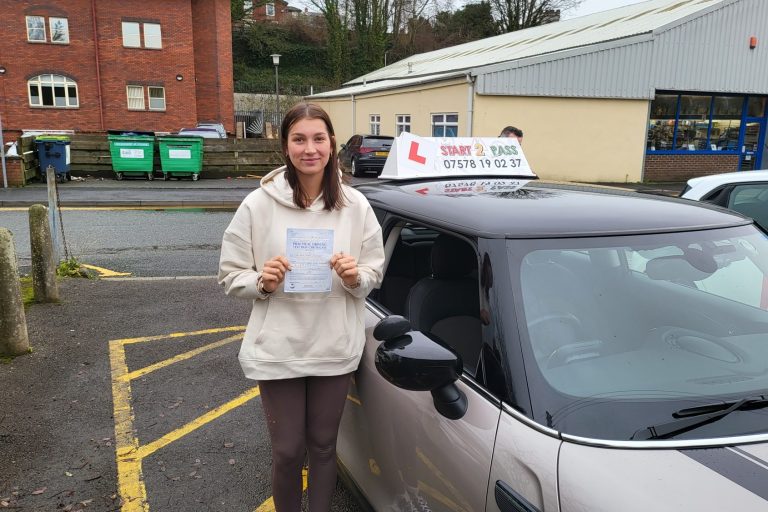 Young woman holding a certificate next to a learner driver car.