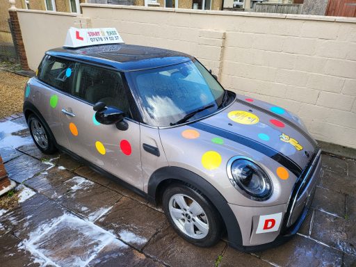 A Mini Cooper car with colourful polka dots and a driving school sign on top.