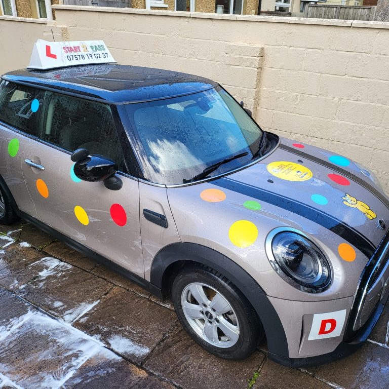 A decorated driving school car with colourful dots for red nose day and L-plates.