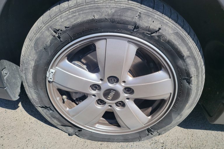 A close-up of a car wheel with a damaged tyre and silver alloy rim.