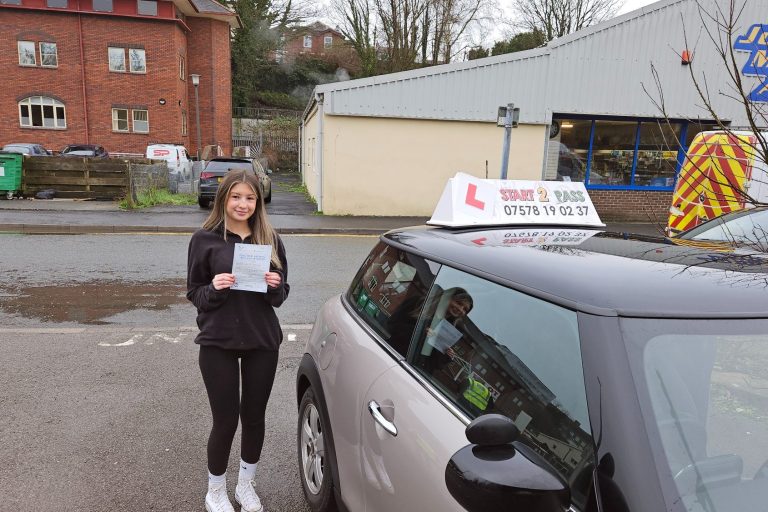 A young woman holding a driving test certificate next to a driving school car.