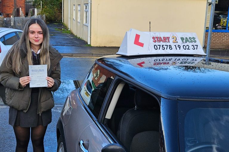 Young woman holding a driving certificate next to a learner driver car.