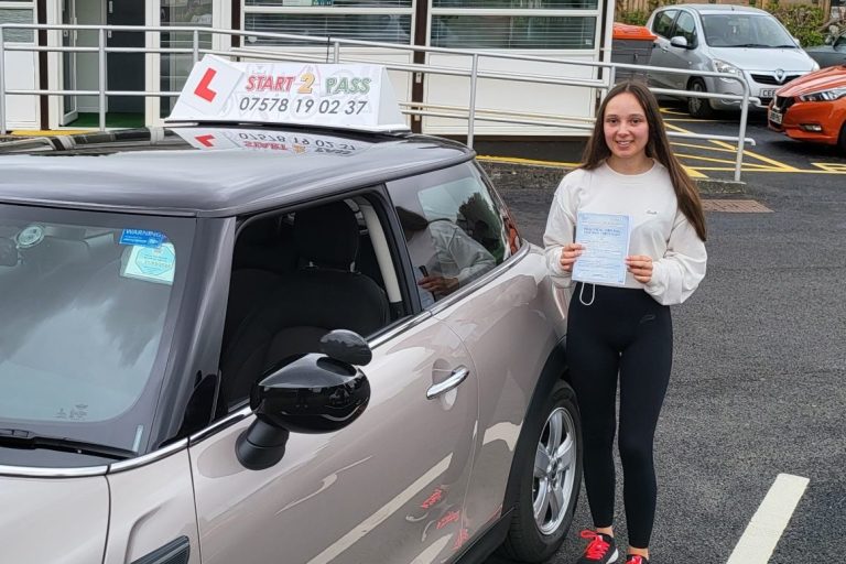 Young woman holding a certificate beside a driving school car in a parking area.