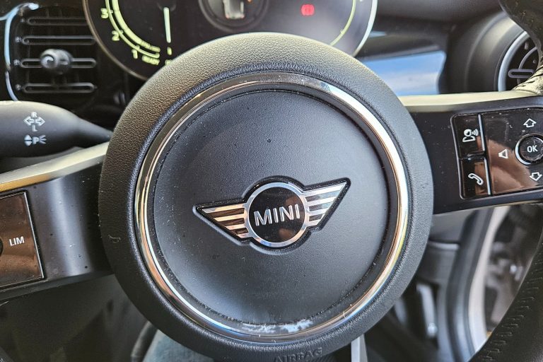 Close-up of a Mini steering wheel with logo and dashboard controls visible.