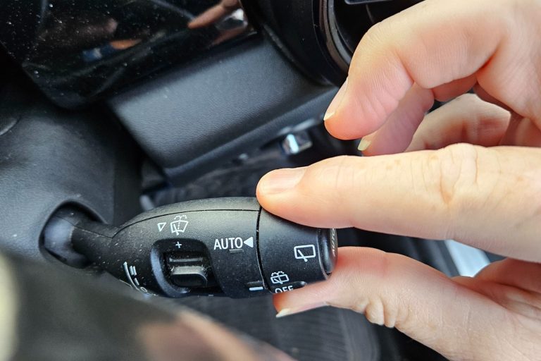 Hand adjusting a car's indicator stalk near the dashboard and controls.