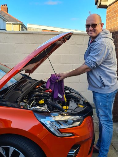 A man in sunglasses is cleaning under the hood of a red car.