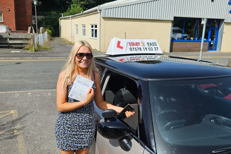 A female driving instructor stands next to a car holding a driving licence.