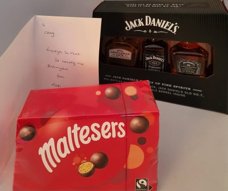 A box of Maltesers chocolates beside a Jack Daniel's gift set and a greeting card.