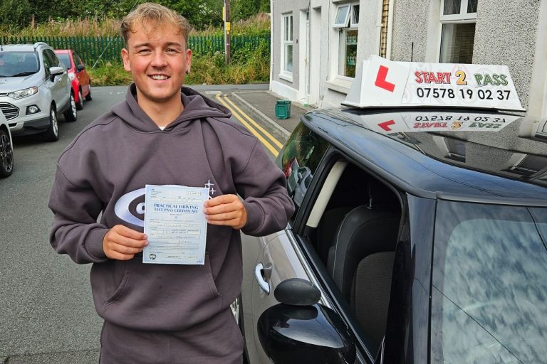 A young man holding a driving certificate beside a learner car.