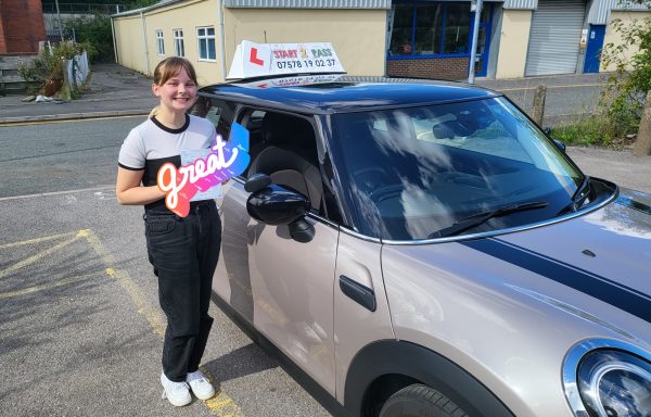 Smiling young woman holding a "Just Passed" sign next to a car with a learner driver sign.