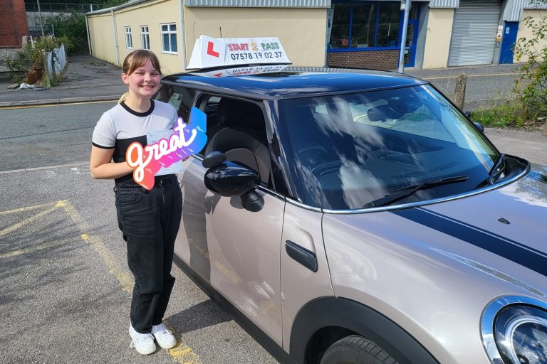 A young woman holds a sign next to a driving school car in a parking lot. passed driving test