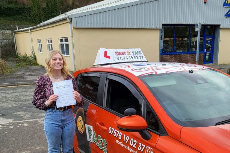 A woman holds her driving test certificate next to a red learner taxi.