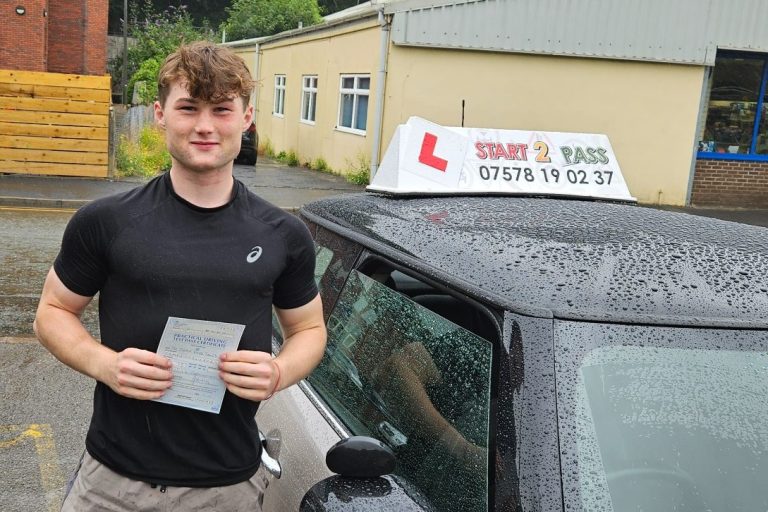 Young man holding a certificate standing next to a car with a driving instructor sign.